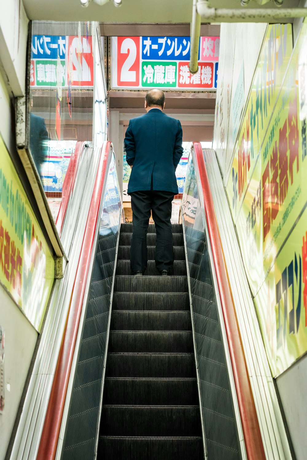 man in blue suit jacket standing on escalator