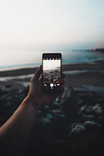 selective focus photography of person taking photo of seashore