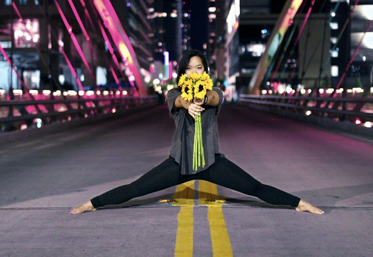 woman holding sunflowers while splitting at the center of road during nighttime