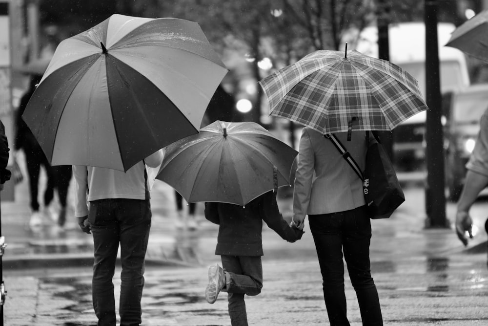 Fotografía en escala de grises de tres personas sosteniendo paraguas