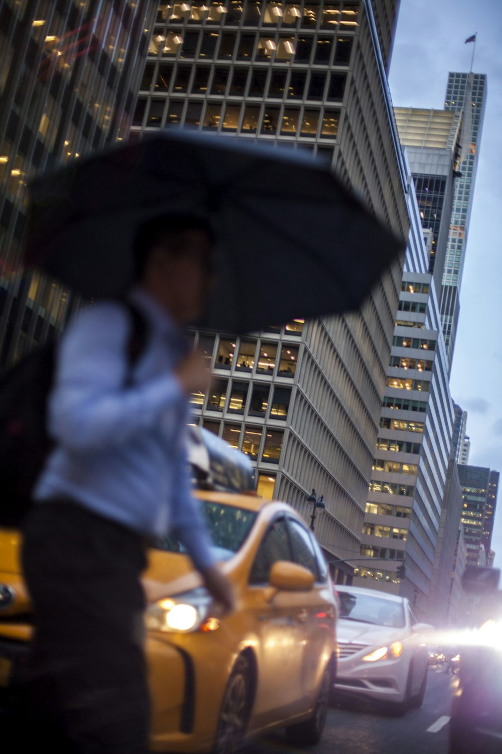 man in blue dress shirt holding umbrella crossing street during daytime