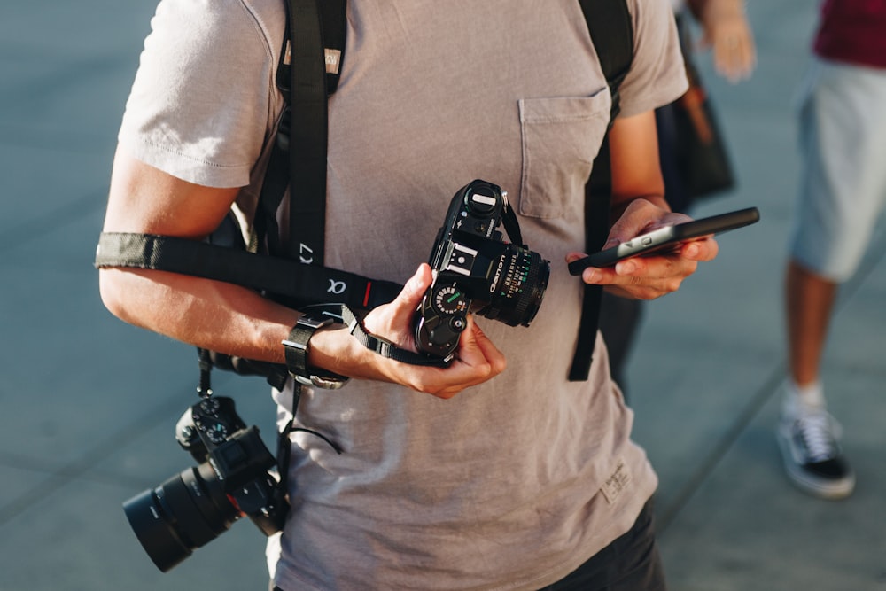 hombres sosteniendo un teléfono inteligente y dos cámaras DSLR