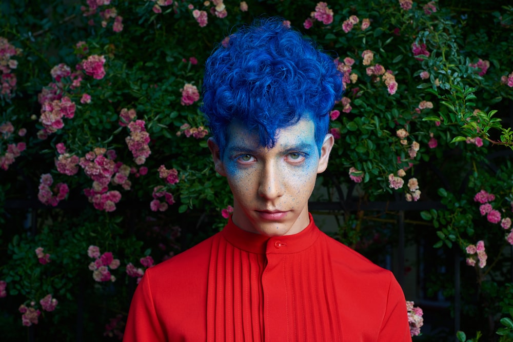 blue haired man standing in front of pink flower plants