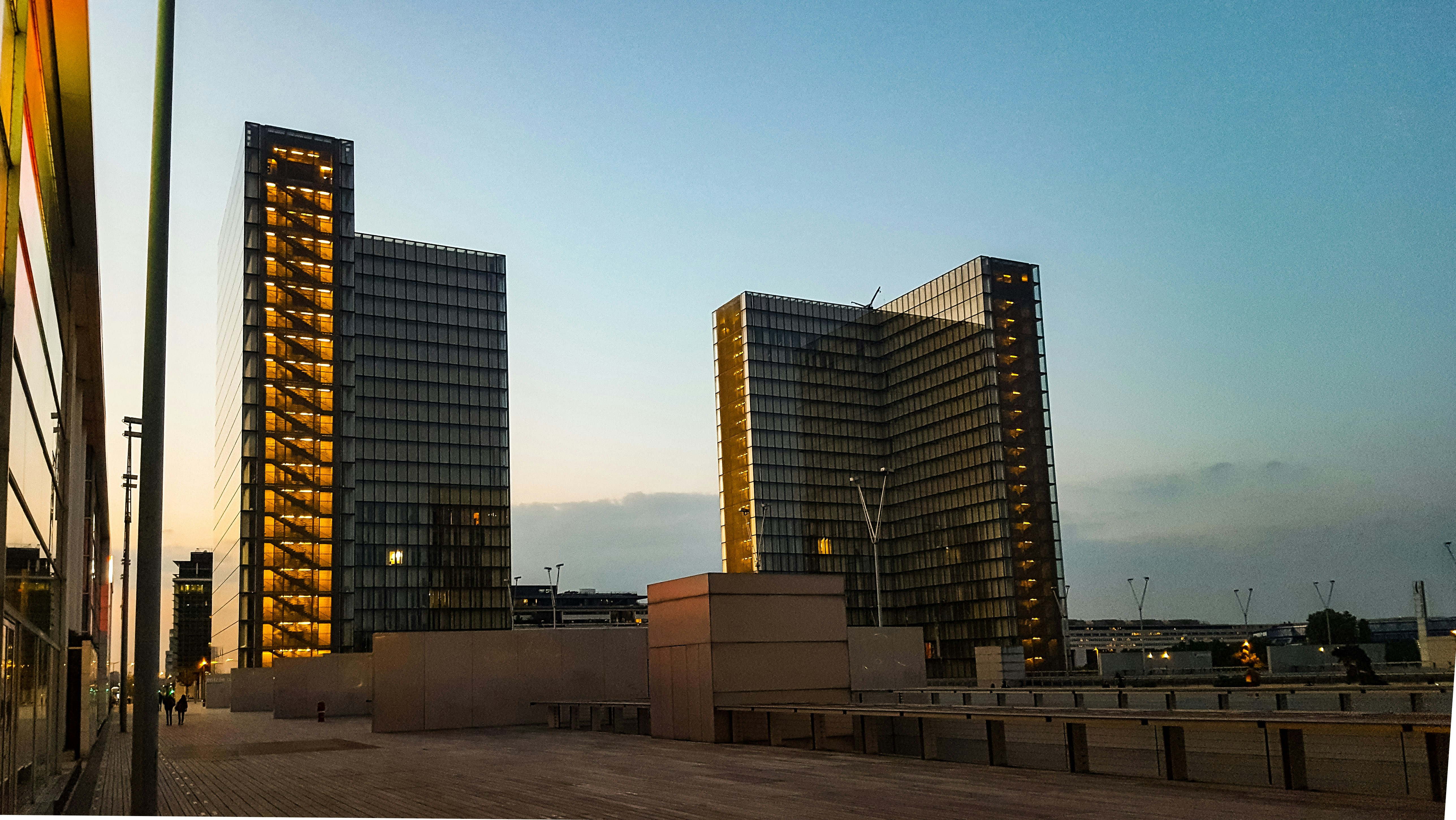 Monumental Abu Dhabi skyline at dusk — towers rising from deep shadow with warm gold atmospheric light and architectural precision