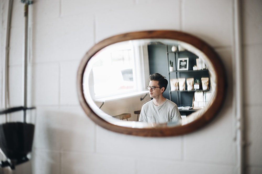 타원형 갈색 나무 액자 거울 선글라스를 착용 한 남자보기