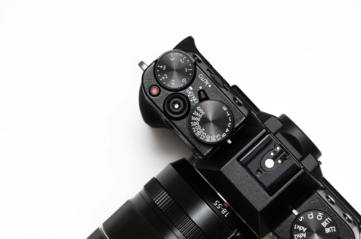 Vue de dessus d'un appareil photo hybride noir avec ses molettes de réglage, sur fond blanc