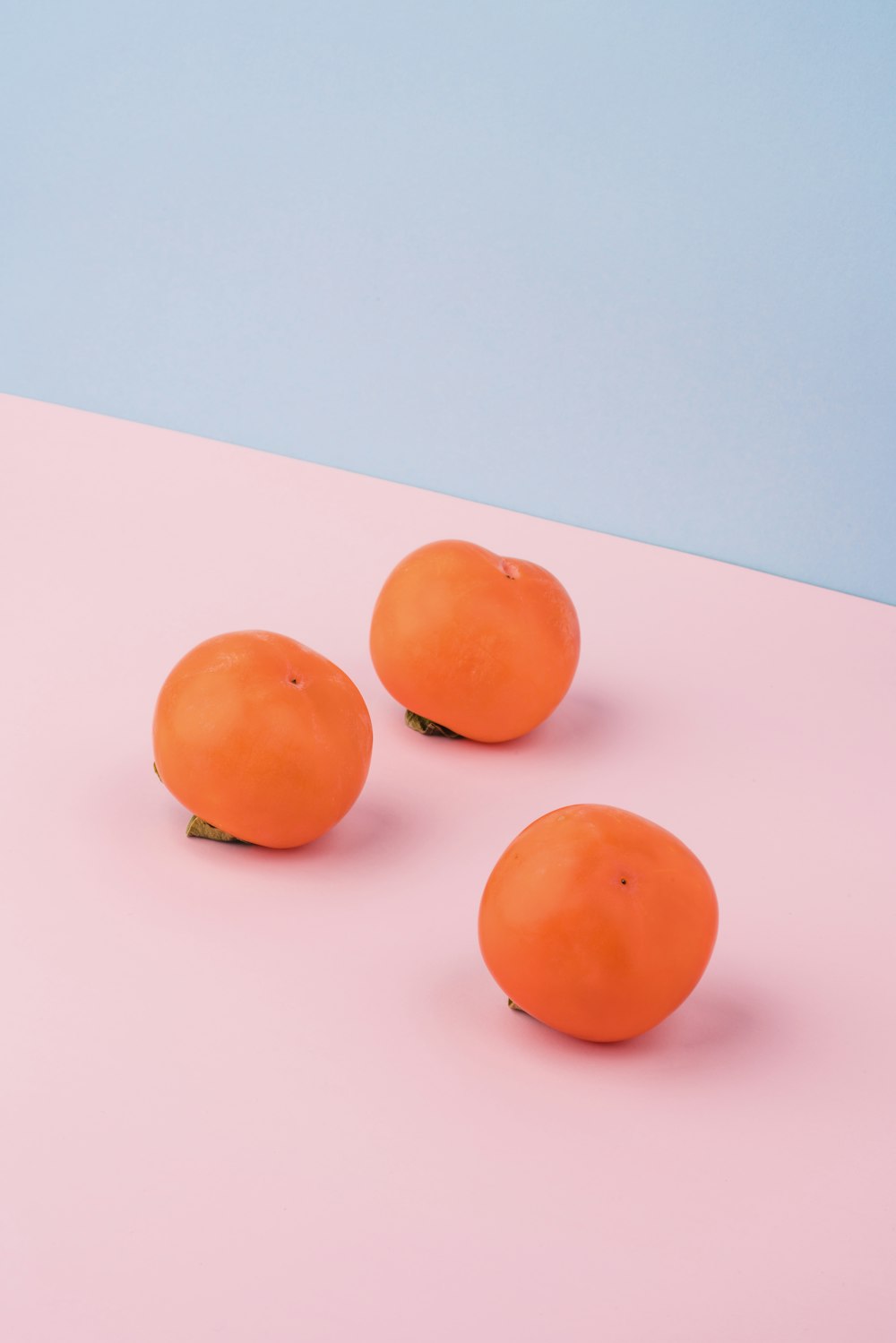 three orange fruits on pink surface