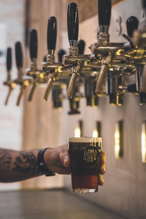 person holding beer mug under keg tap