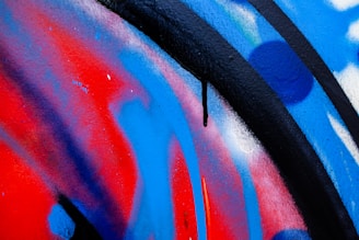 Vibrant graffiti art displaying bold strokes of red, blue, and black, with splashes of white. The artwork features curved lines and patterns, contributing to a dynamic and energetic composition.