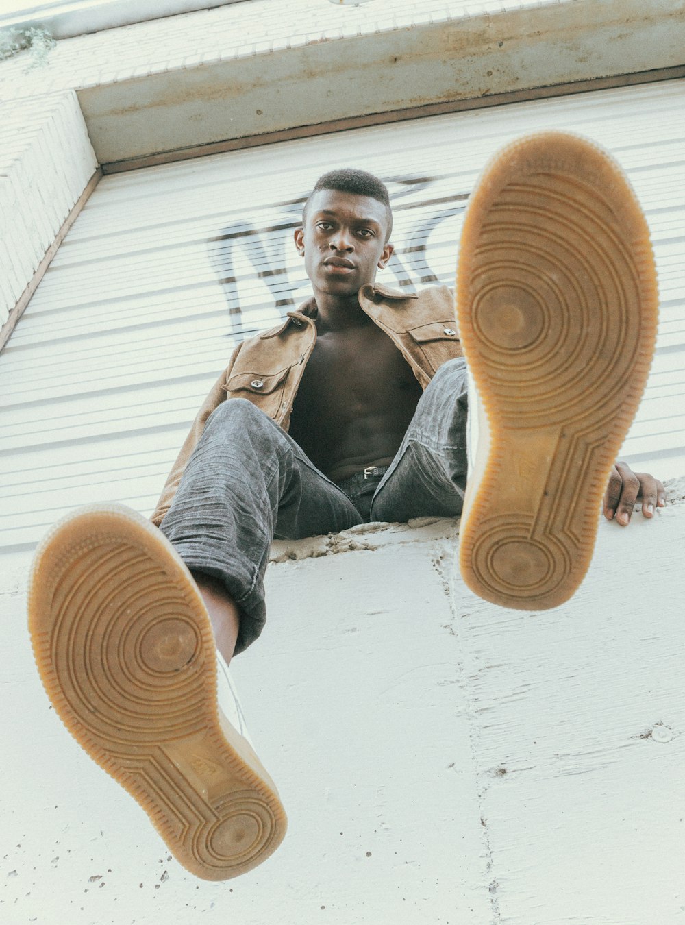 homme en veste marron assis sur un rebord en béton blanc