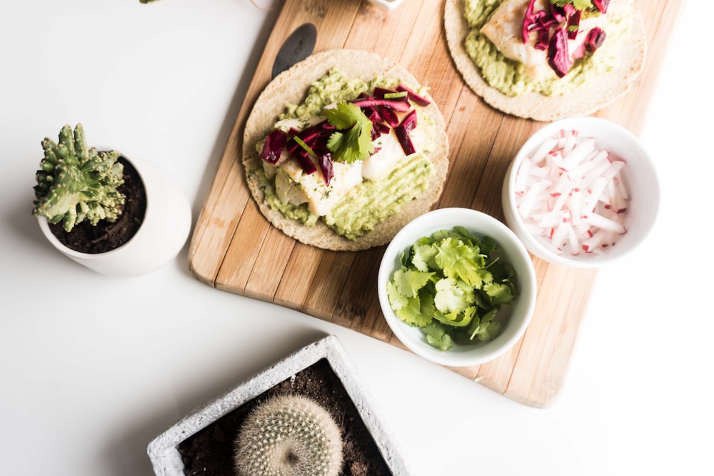 green cacti beside wooden board with foods on white surface