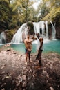 two man standing in front of the waterfalls during daytime