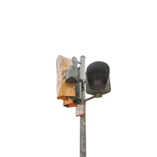 A traffic light mounted on a metal pole. The light is covered, possibly indicating that it is under maintenance or not in use. A small sign with numbers is attached to the pole.