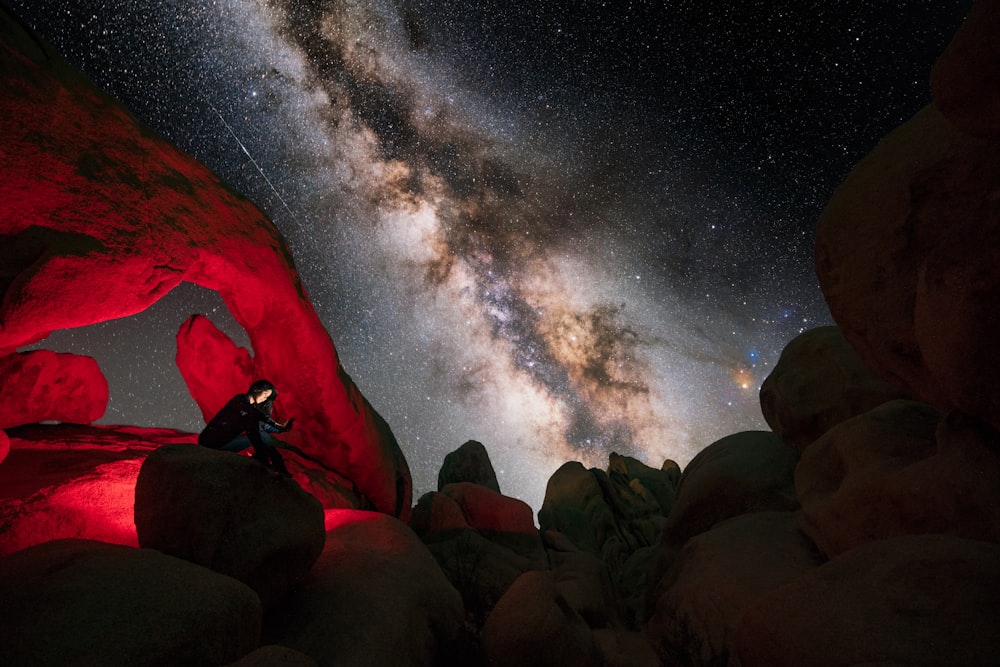 a man standing on a rock under a night sky filled with stars