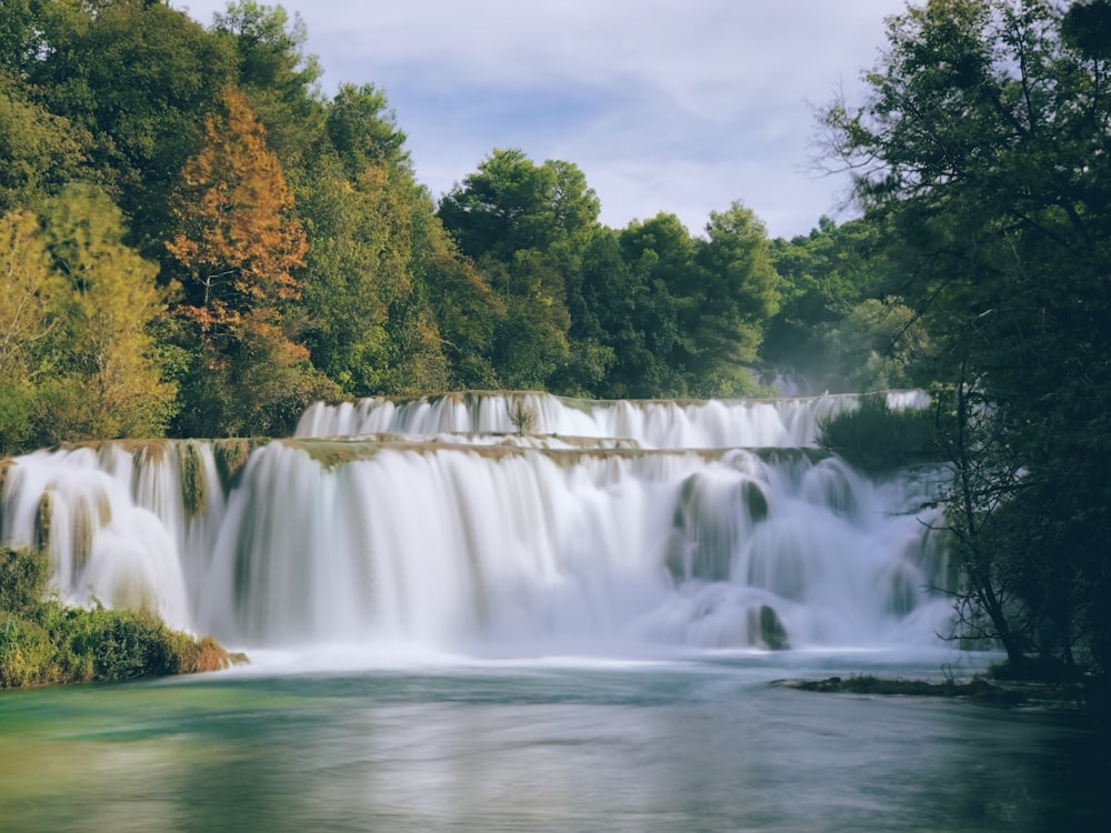 waterfalls with trees under cloudy sky