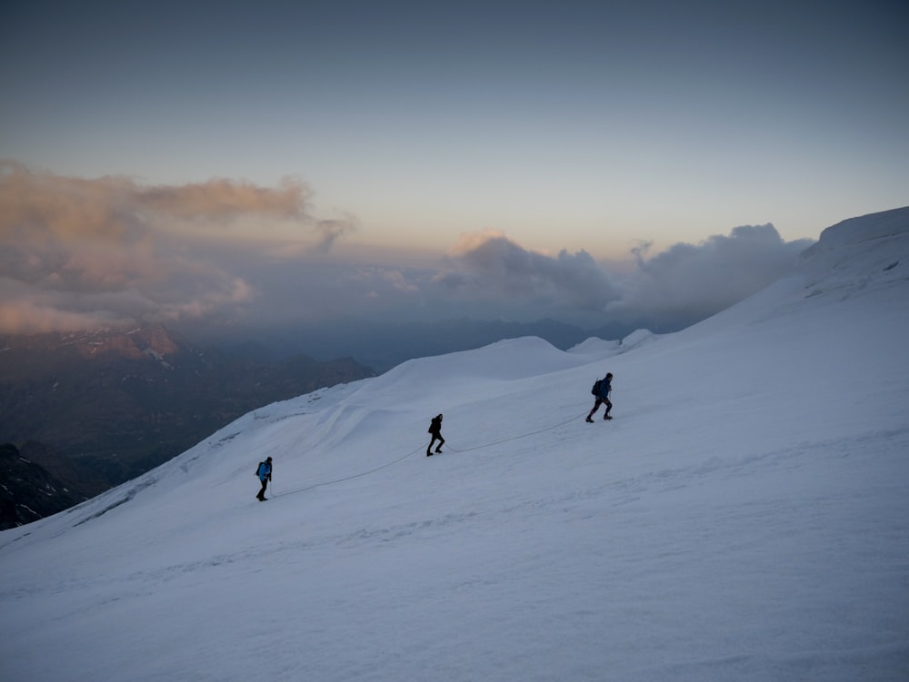three person climbing on snow covered mountain