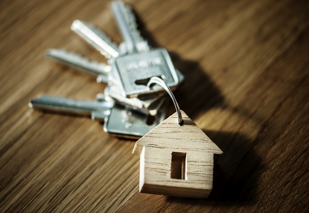 selective focus photography of four silver keys with brown house keychain on brown surface