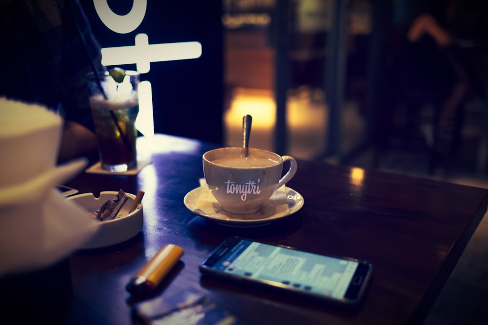 teléfono inteligente Android negro junto a una taza de té en una mesa de centro de madera marrón