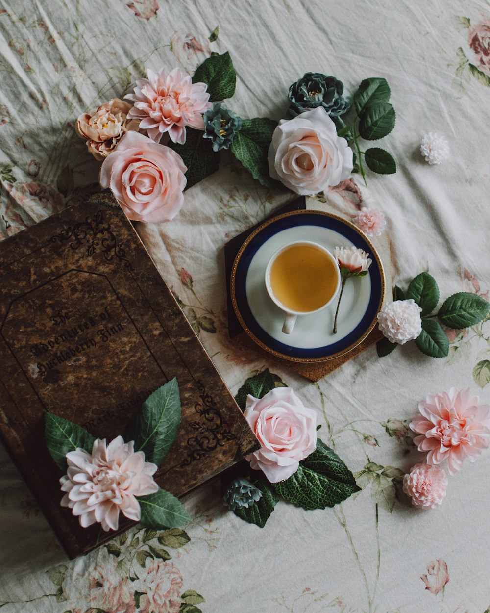 white teacup on plate surrounded pink roses