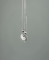Two necklaces with circular pendants form a yin-yang shape. Each half has an engraved design, one labeled 'BEST' and the other 'FRIENDS'. The pendants are metallic with a shiny finish, suspended on thin chains against a plain gray background.