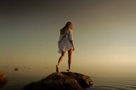 woman walking over brown rocks near body of water during daytime