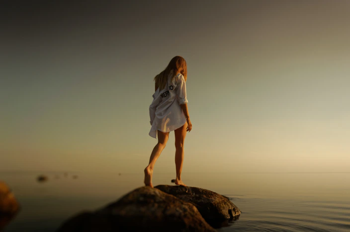 woman walking over brown rocks near body of water during daytime