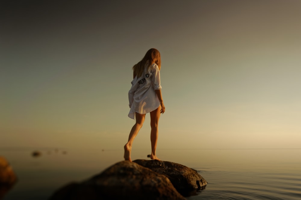 Donna che cammina su rocce marroni vicino allo specchio d'acqua durante il giorno