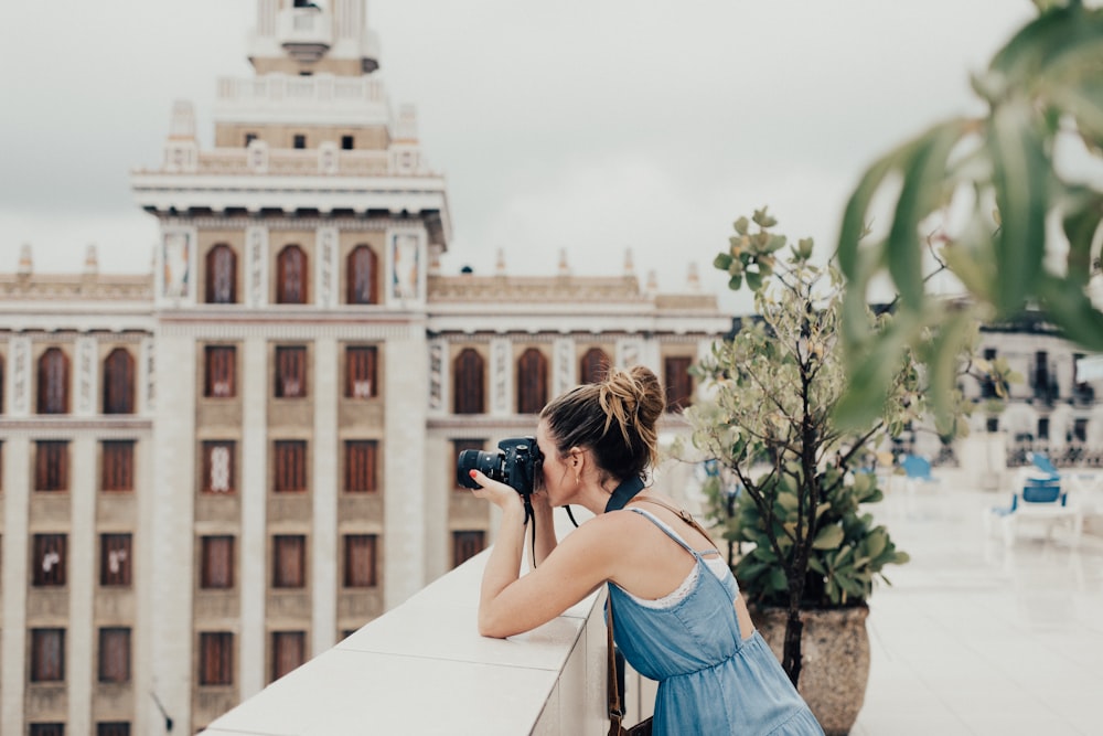 woman leaning on beige surface holding camera