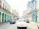 Smiling woman enjoying a colorful Cuban street with vintage cars.