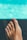 A foot with toenails painted in a bright color is in focus against a blurred background. The background features shades of turquoise, suggesting water, possibly from a pool.