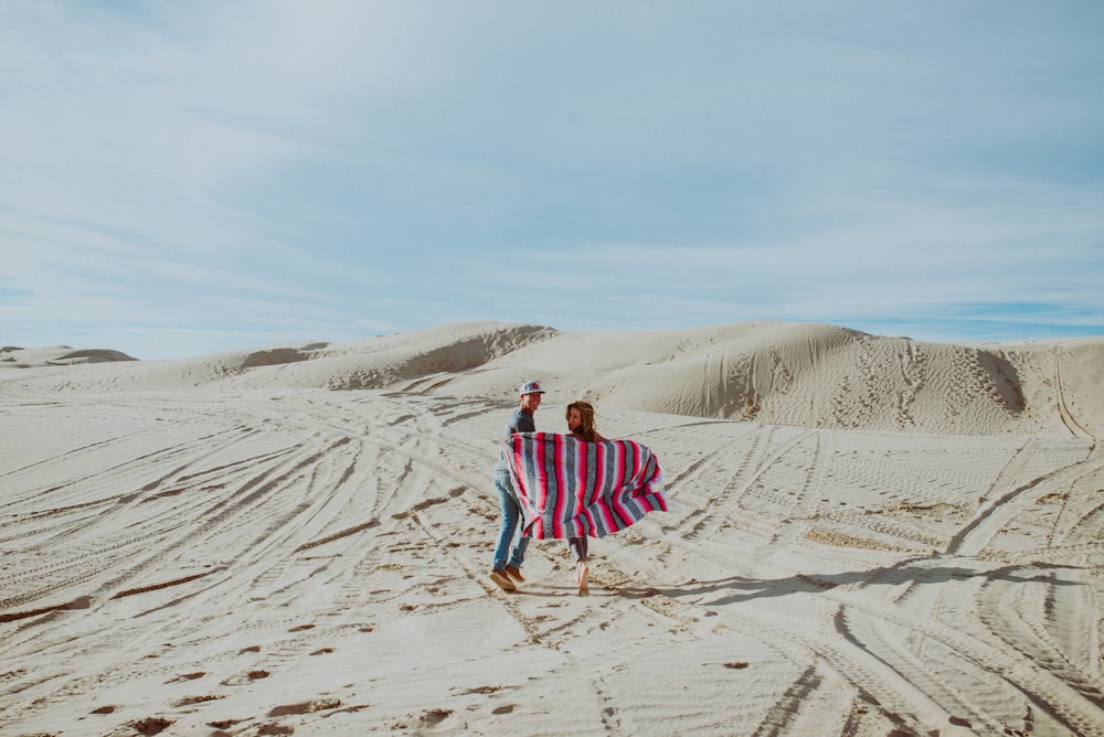 man standing beside woman holding scarf in desert