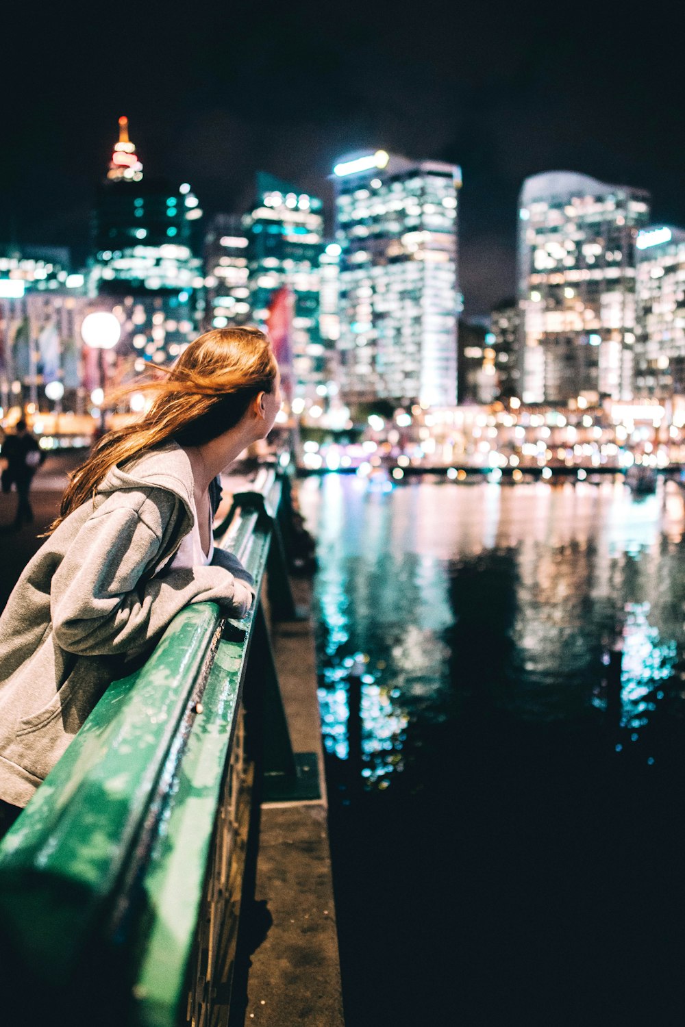 woman holding green metal bridge fence looking on building