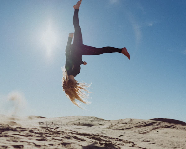 A woman mid back-flip under a blue sky