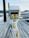 An electrical outlet station with multiple yellow power sockets is mounted on a wooden dock. Thick grey cables are coiled around the base of the station, with one yellow plug prominently hanging. In the background, calm water and blurry outlines of hills can be observed. The overall setting suggests a marina or docking area.