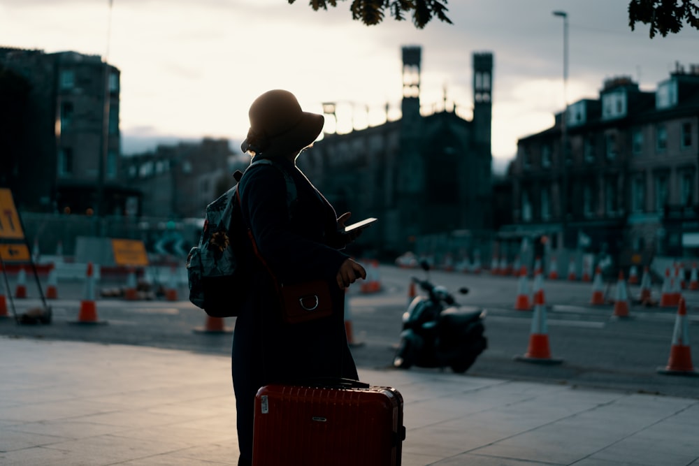 woman wearing coat standing on road with travel luggage during daytime