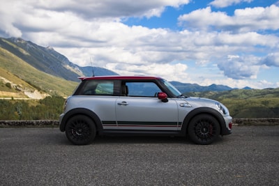 A compact hatchback gleaming in the sunlight, set against a scenic mountain highway.