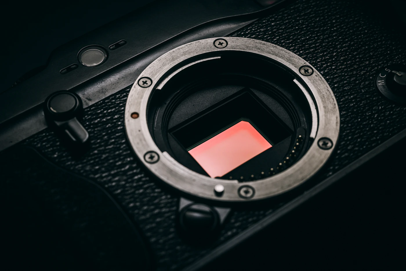 A mirrorless camera body with no lens fitted, showing the sensor glowing orange-pink inside the mount