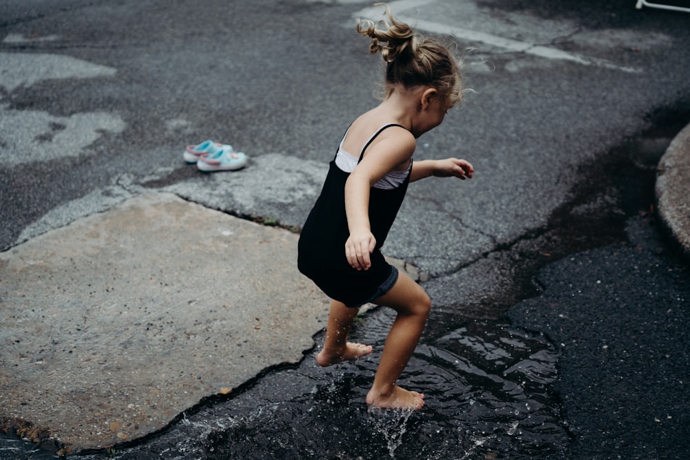 La niña salta en la superficie del agua en la carretera de asfalto durante el día