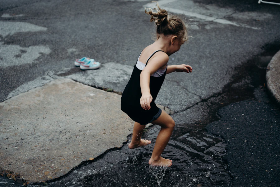 Young girl in boots jumping and splashing in a puddle outdoors