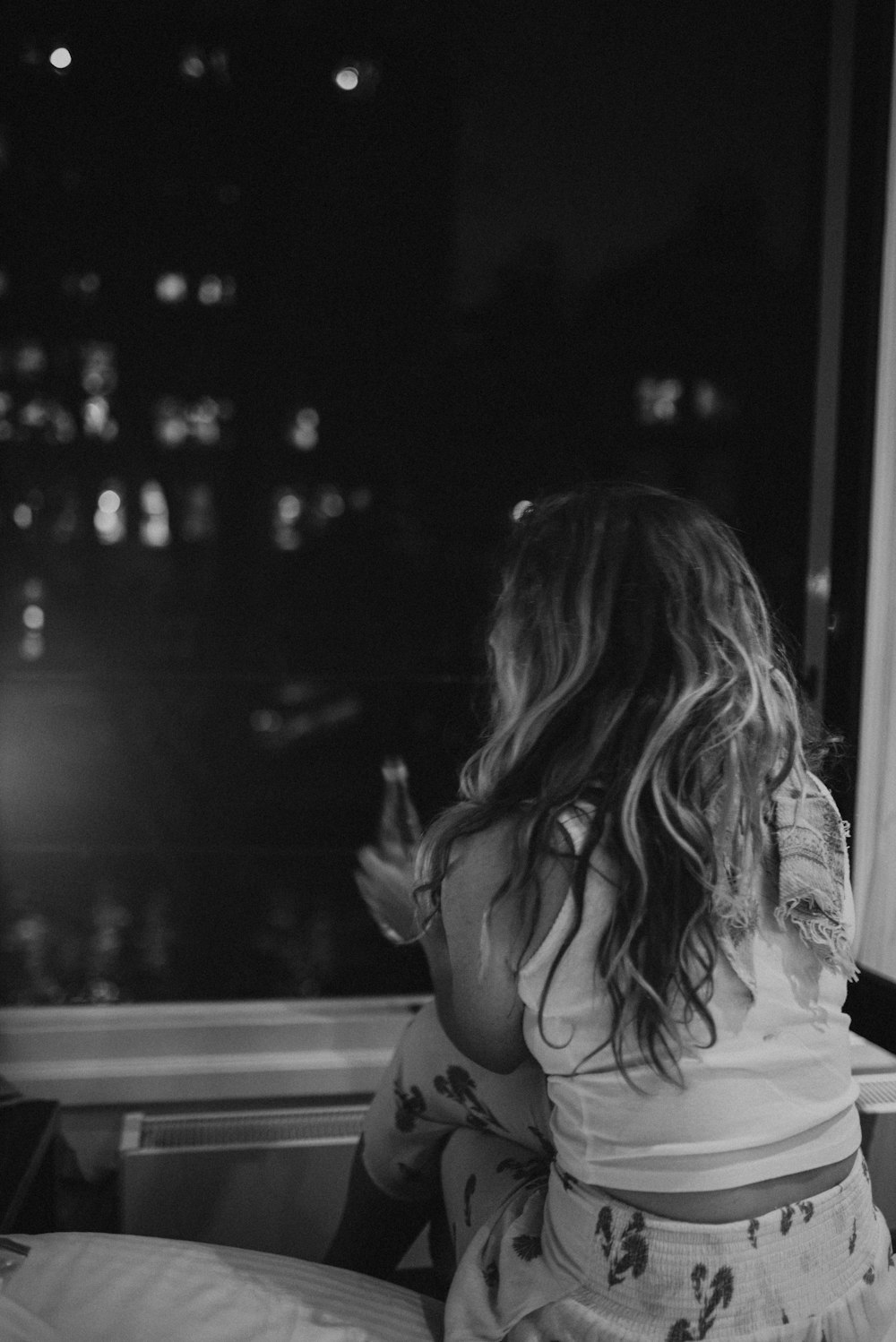 woman sitting and holding beverage bottle facing opened window during night