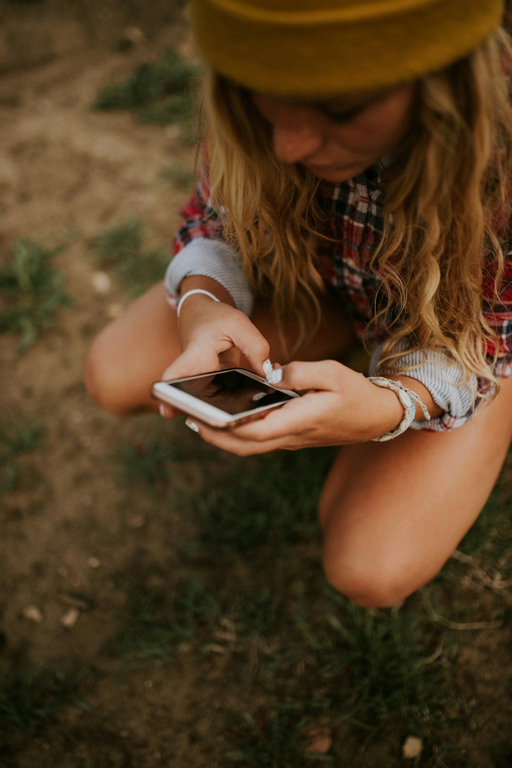 woman squatting on grass field while using white smartphone