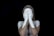 A person with light skin is standing against a black background, covering their face with hands that are painted white, extending the white paint to parts of their arms and shoulders.