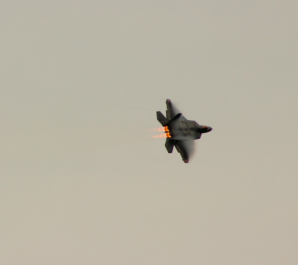 A black jet fighter speeding across grey sky. 