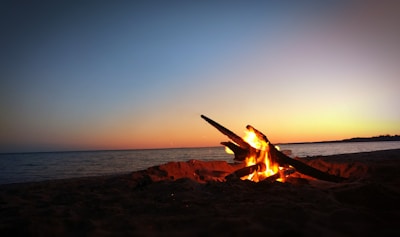 A cozy campfire glowing warmly on a sandy beach at sunset, with marshmallows roasting on sticks.