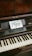 A wooden upright piano displays a small sign on its music stand, inviting interaction with the words 'Go Ahead Play Me' in artistic lettering. The piano has visible keys and a nameplate reading 'CAROL OTTO BERLIN'.