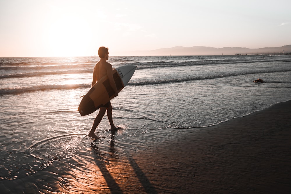 Person mit Surfbrett, die am Meeresufer spazieren geht