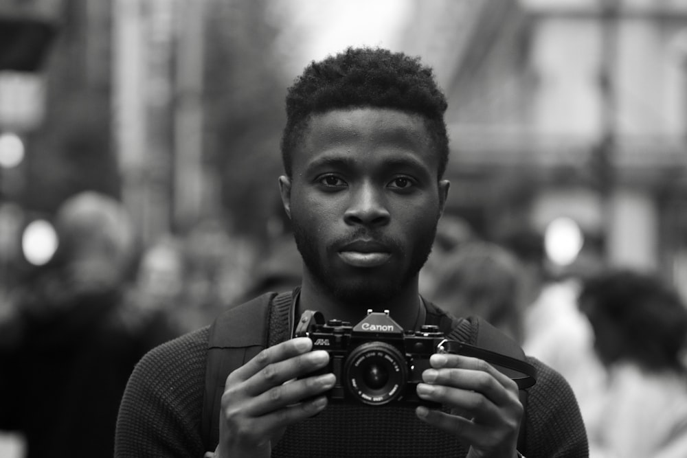 grayscale photo of man holding Canon camera