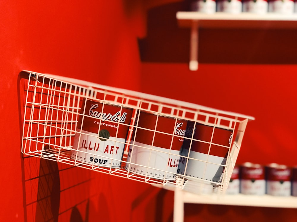 Un mur rouge avec un panier en fil de fer blanc contenant des canettes de coca - Cola