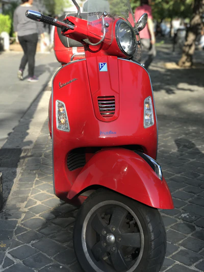 A shiny red electric scooter parked by a city sidewalk bathed in morning light.