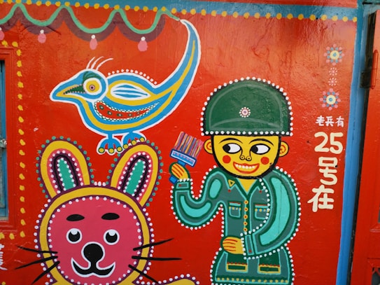 A vibrant mural painted on a wall, featuring a stylized soldier holding a brush, a colorful cartoon bird, and a whimsical rabbit. Intricate dotted patterns in various colors accentuate the figures, and there are decorative floral motifs and Chinese text.